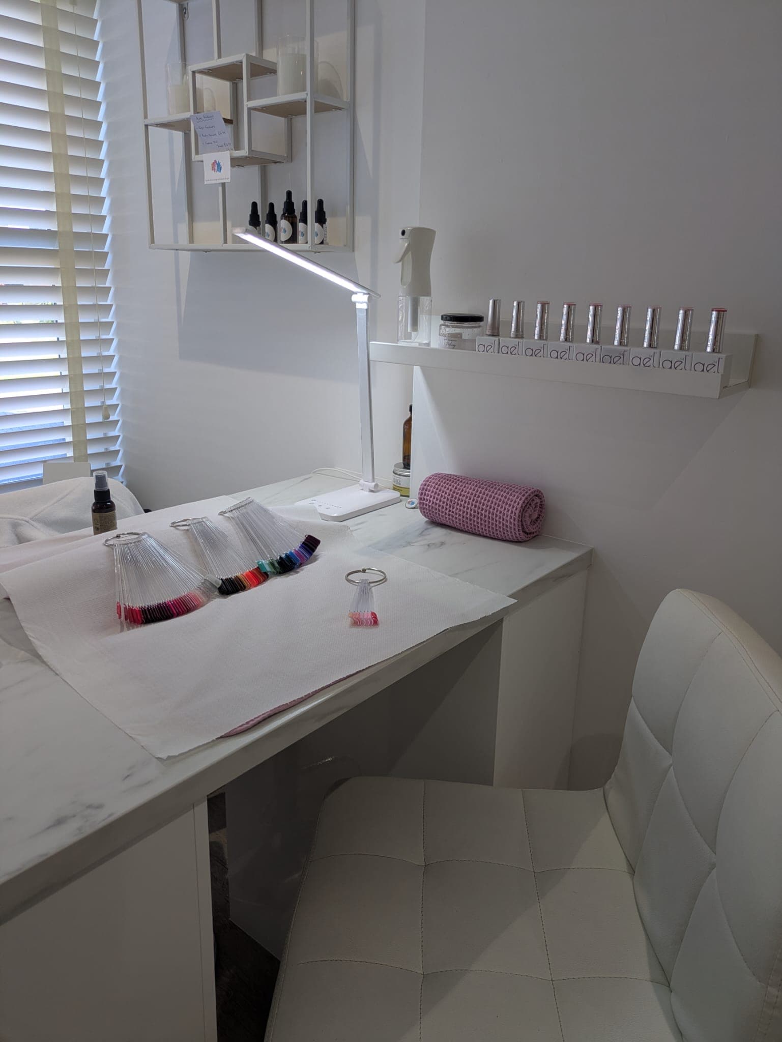 Aura's manicure desk with nail colour samples, a task lamp and a white padded chair beside the window