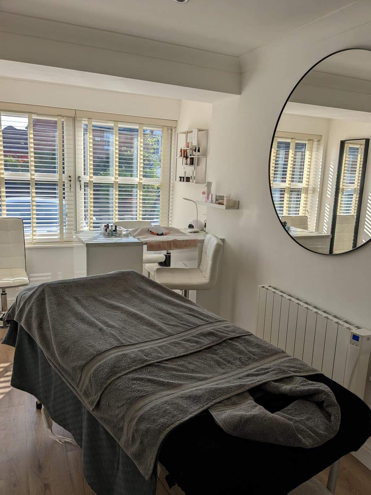 The treatment couch made up with towels, beside the window blinds and round mirror